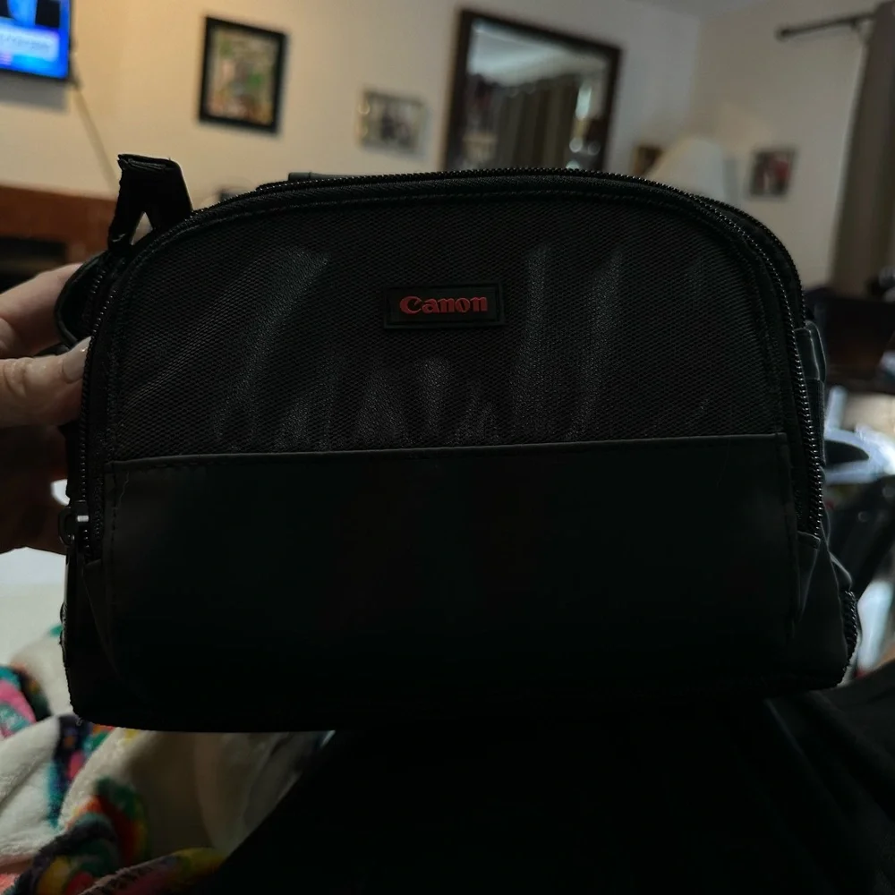 Canon black camera bag with zipper packets, and a handle at the top.